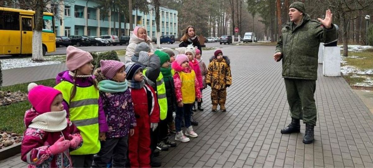 дети дошкольного возраста слушают военного во дворе военной части
