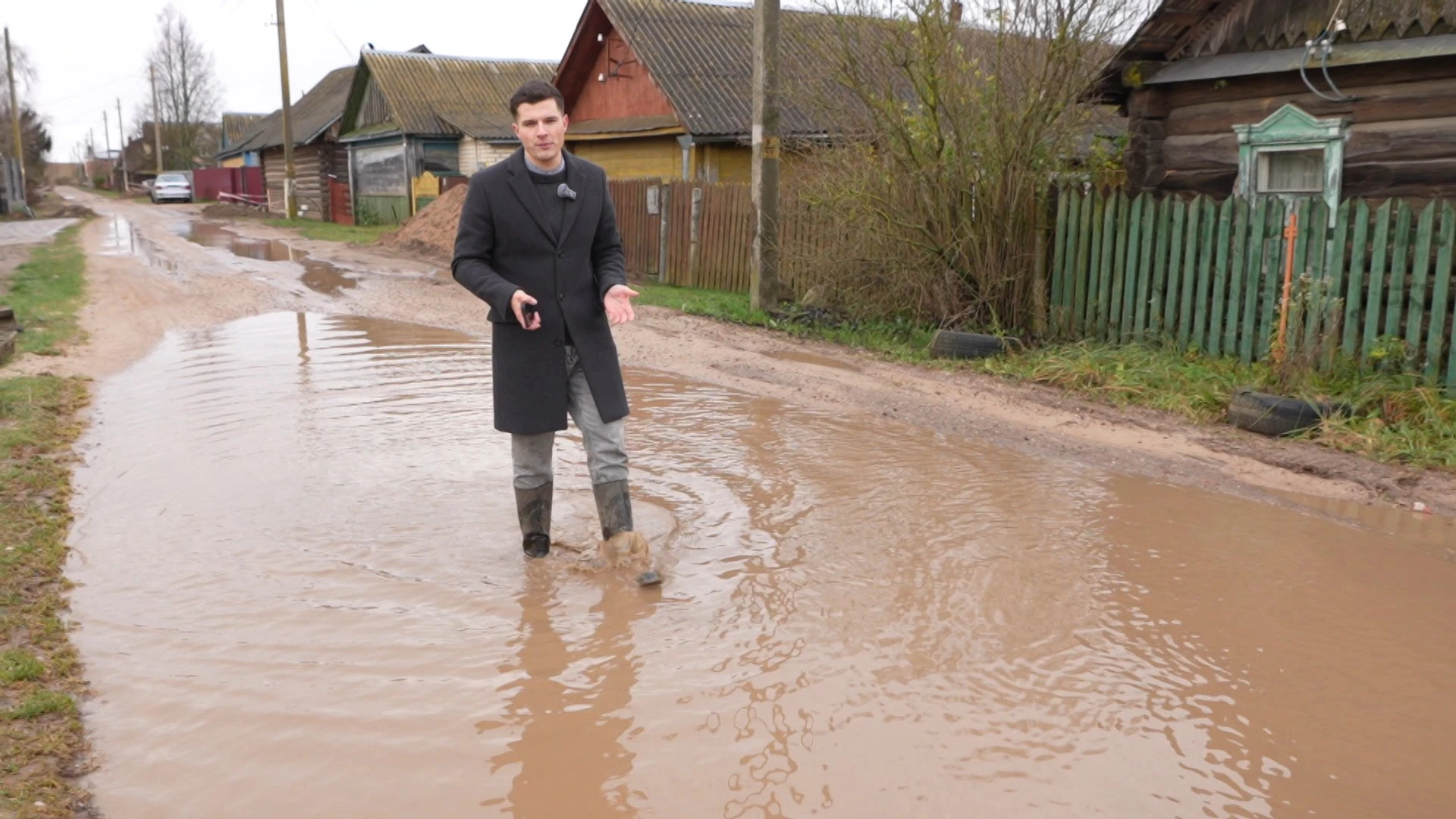 Журналист госканала «Беларусь 1» идет по луже на проблемной улице Пережира.