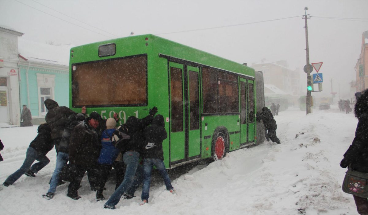 люди толкают автобус в снегопад